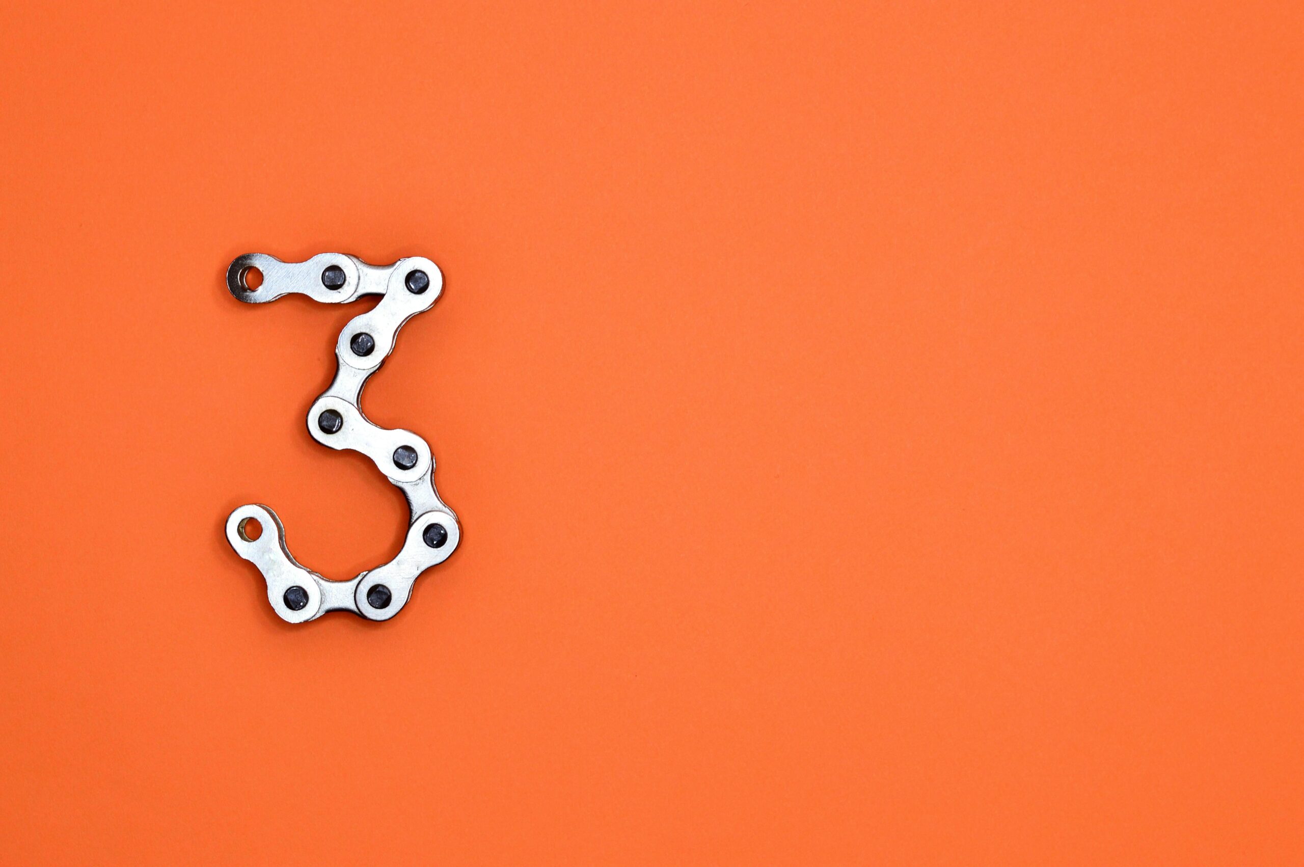 A bicycle chain forms the number three against a vibrant orange backdrop, offering ample copyspace.