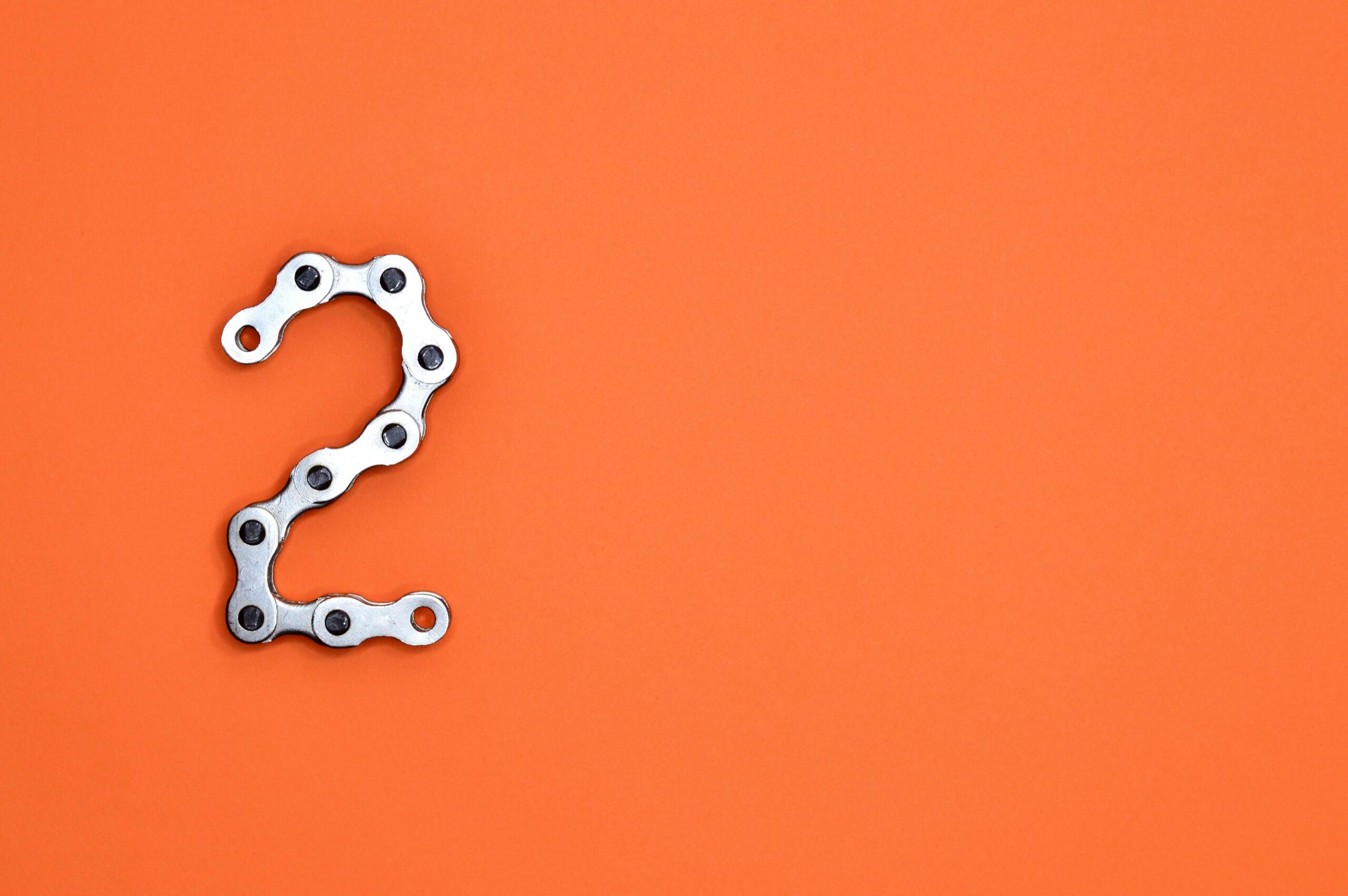 Metal chain forming the number 2 on a bright orange background, perfect for design projects.