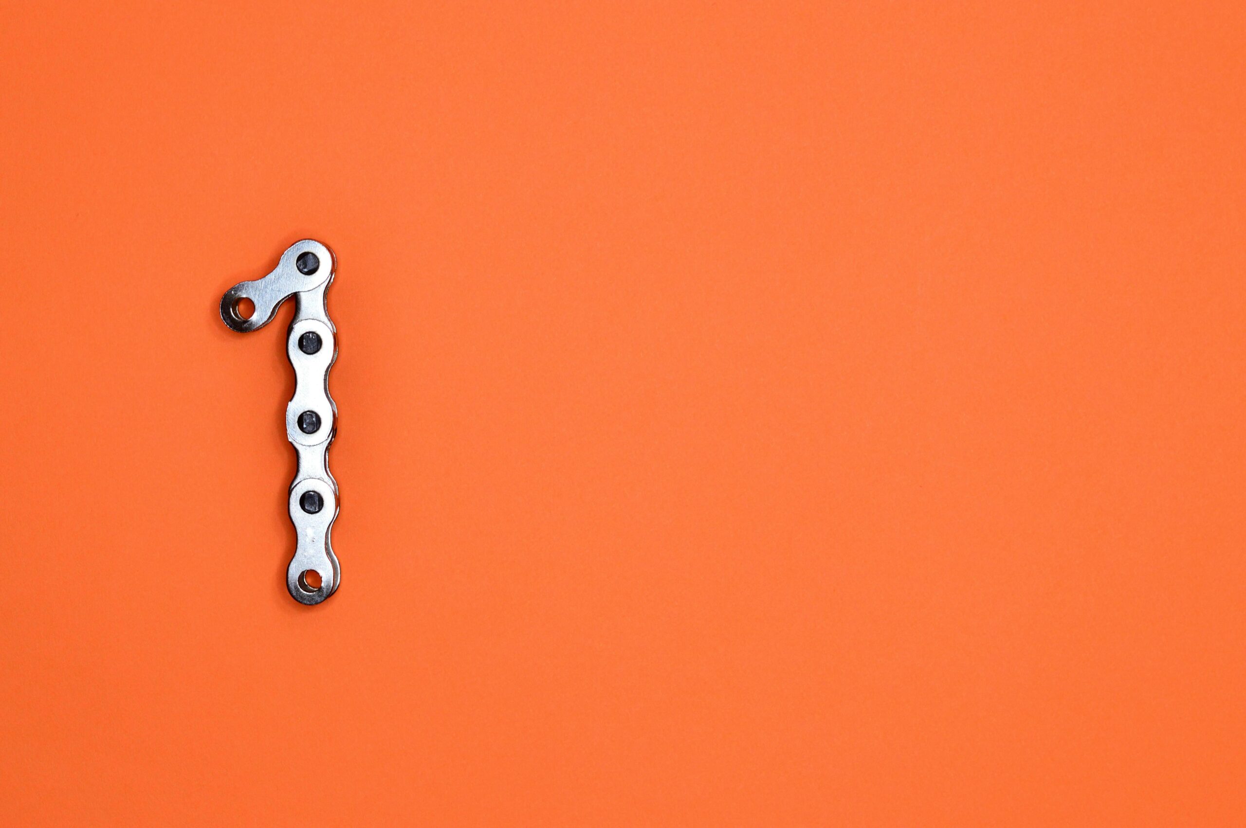 Metal chain forming the number one on an orange background, ideal for design concepts.